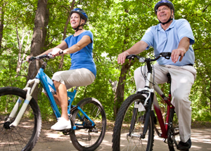 Man and woman riding bicycles on path in woods.